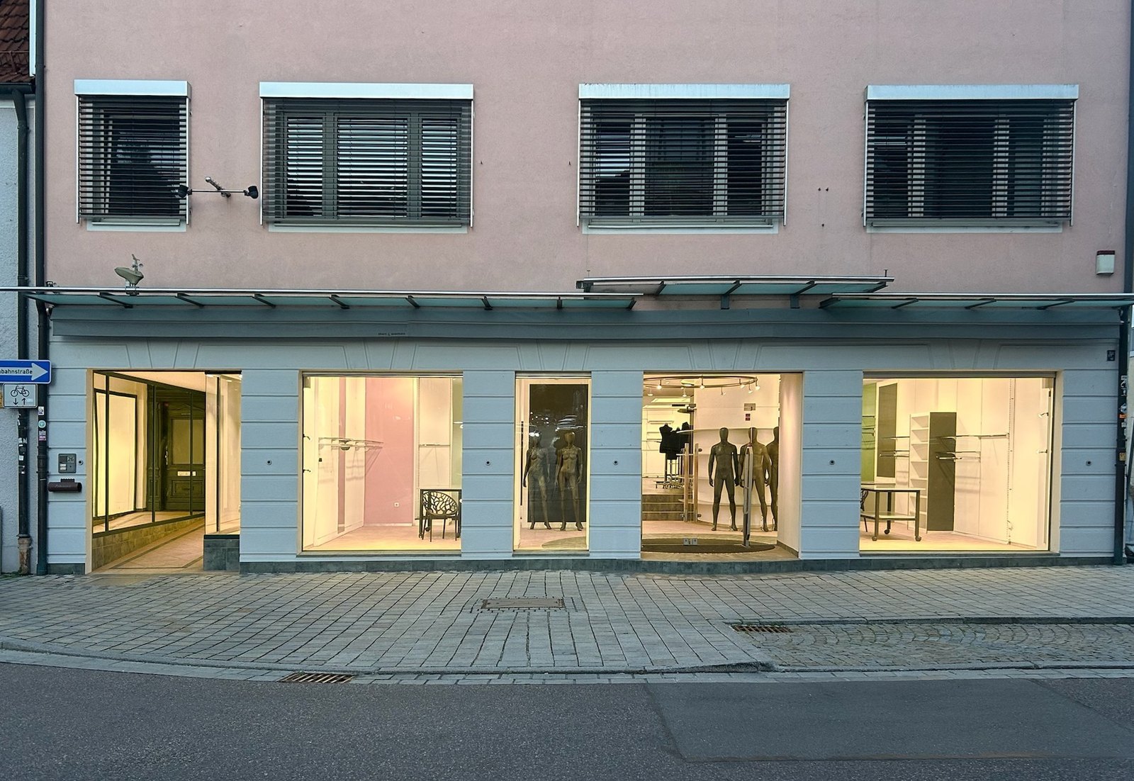 Fassade des Wohn- und Geschäftshauses Frauenstraße 26 in der Abenddämmerung, alle Schaufenster und die Passage beleuchtet